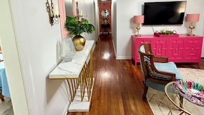 A hallway with a dining table, chairs, a pink cabinet, a television, and a plant.