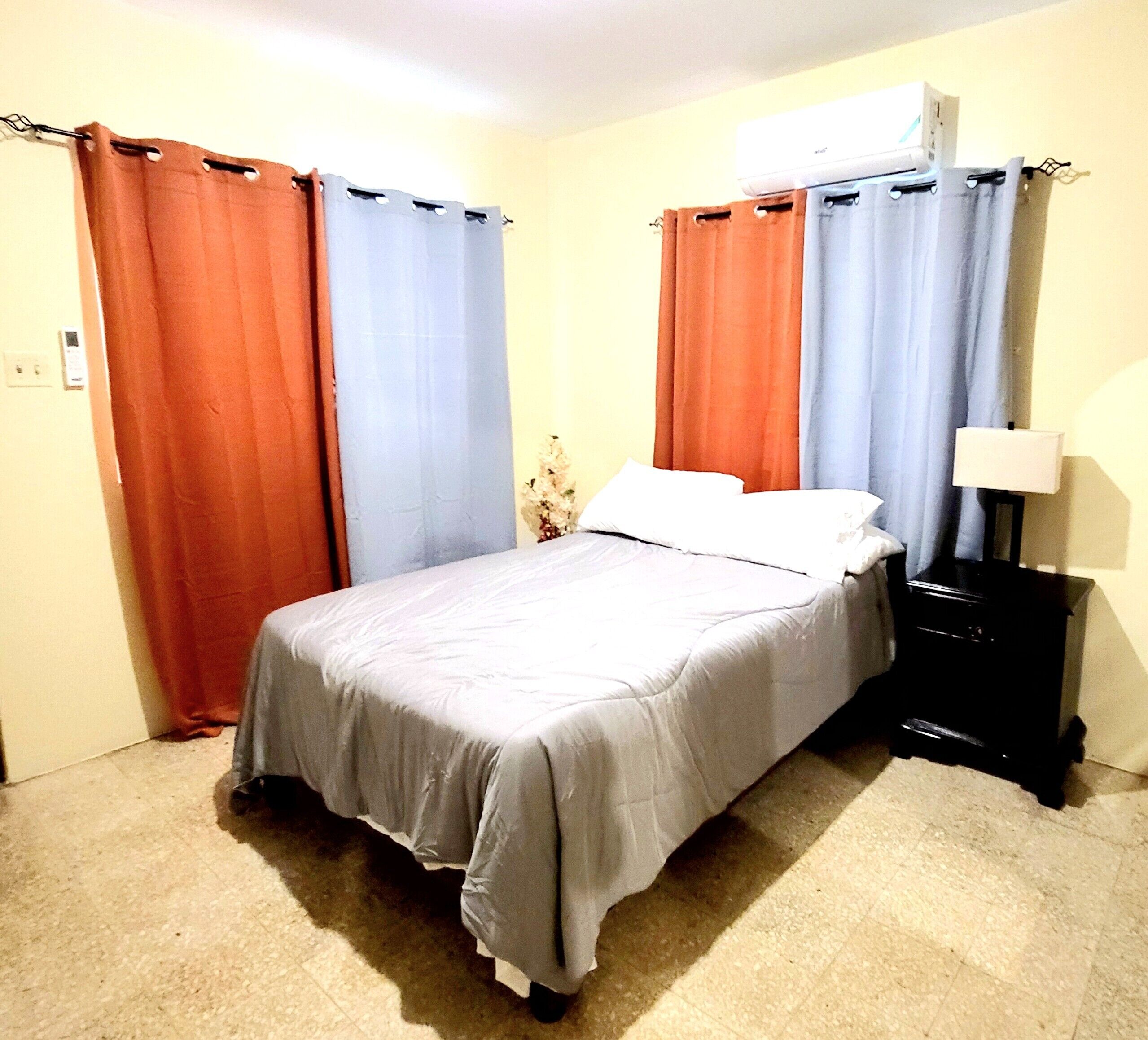 Een slaapkamer met een bed, gordijnen, een nachtkastje en een airconditioning.