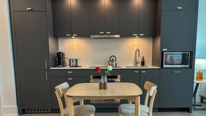 A modern kitchen with dark cabinets, a wooden dining table, and two chairs. - Executive Luxury Suite | The Well Toronto (Toronto)