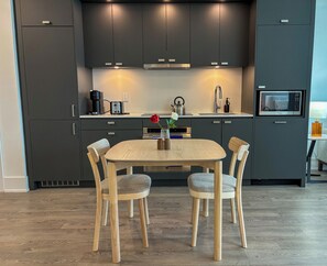 Uma cozinha moderna com armários escuros, uma mesa de jantar de madeira e duas cadeiras.