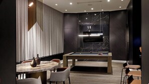 A modern room with a pool table, seating area, and a flat-screen TV mounted on a marble wall. - Executive Luxury Suite | The Well Toronto (Toronto)