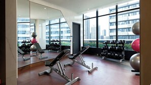 A gym with exercise equipment, a large mirror, and a view of buildings through large windows. - Executive Luxury Suite | The Well Toronto (Toronto)