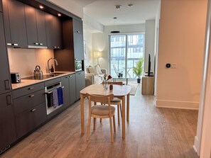A modern kitchen with grey cabinets, a wooden dining table, and a view of the balcony. - Executive Luxury Suite | The Well Toronto (Toronto)