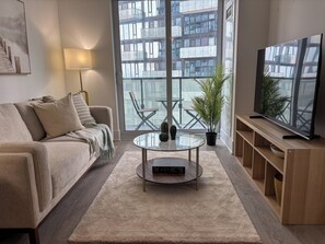 Ein modernes Wohnzimmer mit einer Couch, einem Couchtisch, einem Fernseher und einem großen Fenster mit Blick auf ein Gebäude.