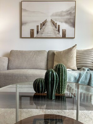 Ein Wohnzimmer mit einer Couch, einem Glastisch mit dekorativen Vasen und einem gerahmten Landschaftsbild an der Wand.