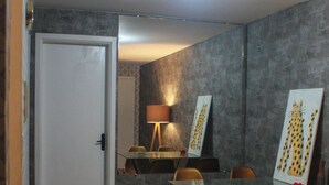 A dining area with a glass table, orange chairs, a lamp, and artwork on the wall.
