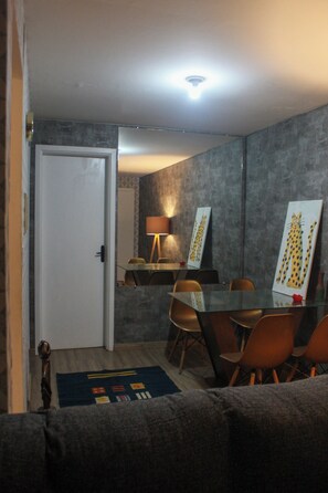 A dining area with a glass table, orange chairs, a lamp, and artwork on the wall.