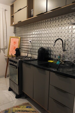 Una cocina con estufa a gas, un lavamanos y salpicadero de azulejos.