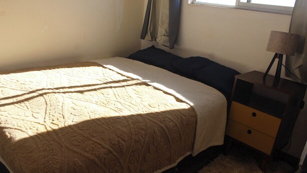 A bedroom with a bed, a nightstand, a lamp, and a window with curtains.