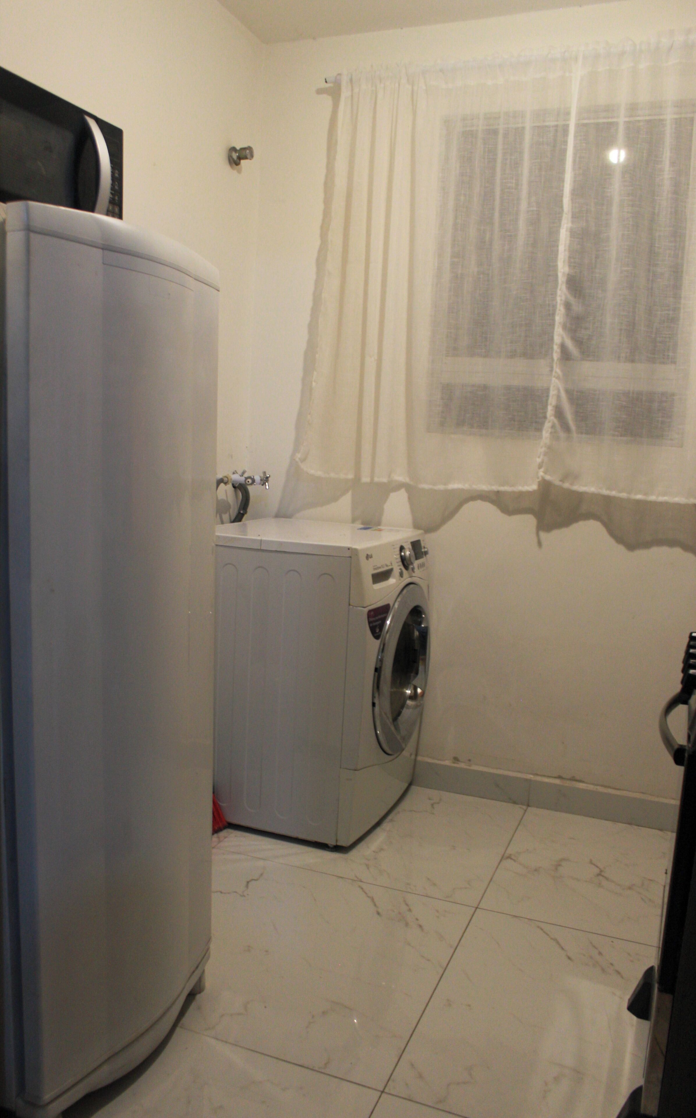 Un lavadero con una lavadora y un electrodoméstico blanco grande, posiblemente una secadora o lavadora, sobre un piso de baldosas.