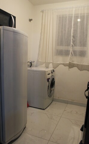 A laundry room with a washing machine and a large white appliance, possibly a dryer or washer, on a tiled floor.