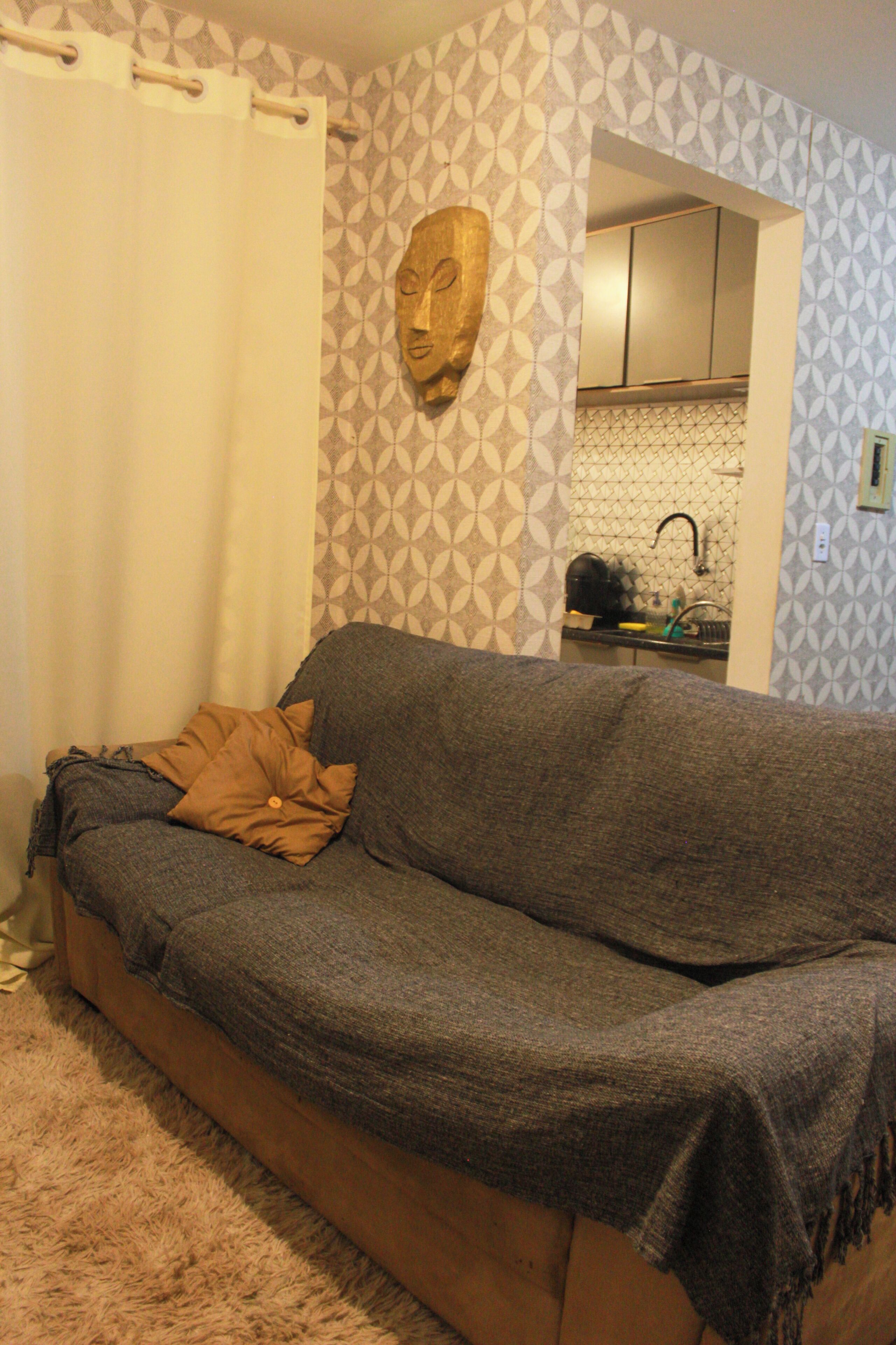 A living room with a sofa, a patterned wall, and a kitchen visible through an open doorway.