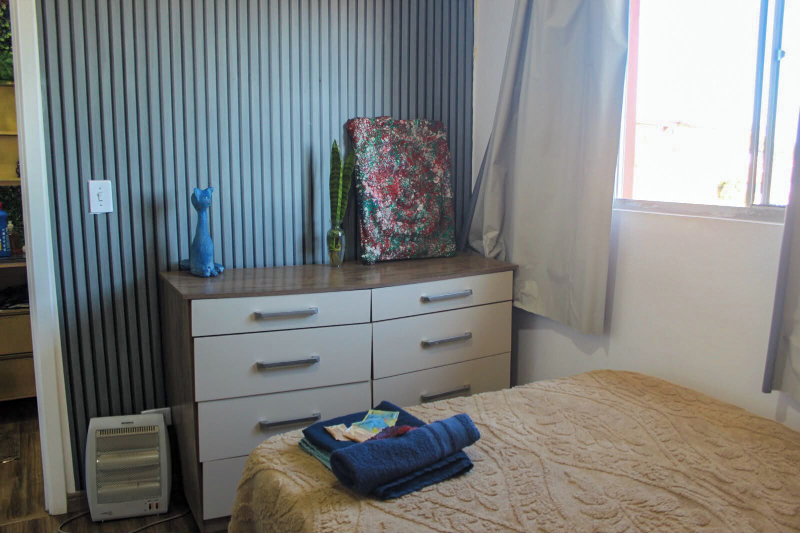 Quarto com cama, penteadeira, radiador e janela com cortinas.