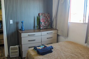 Un dormitorio con cama, cómoda, radiador y ventana con cortinas.