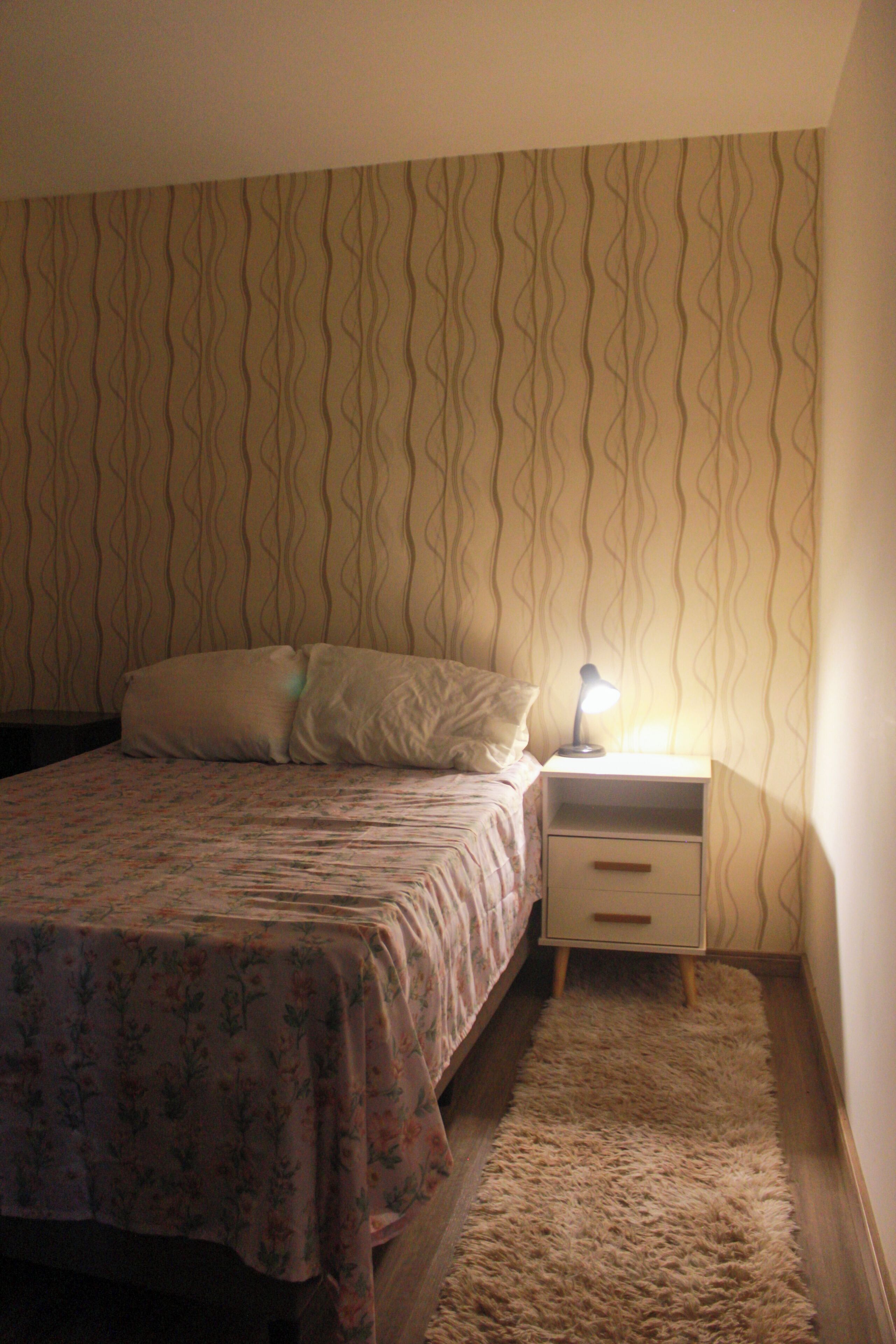 A bedroom with a bed, a nightstand, a lamp, and a patterned wall.