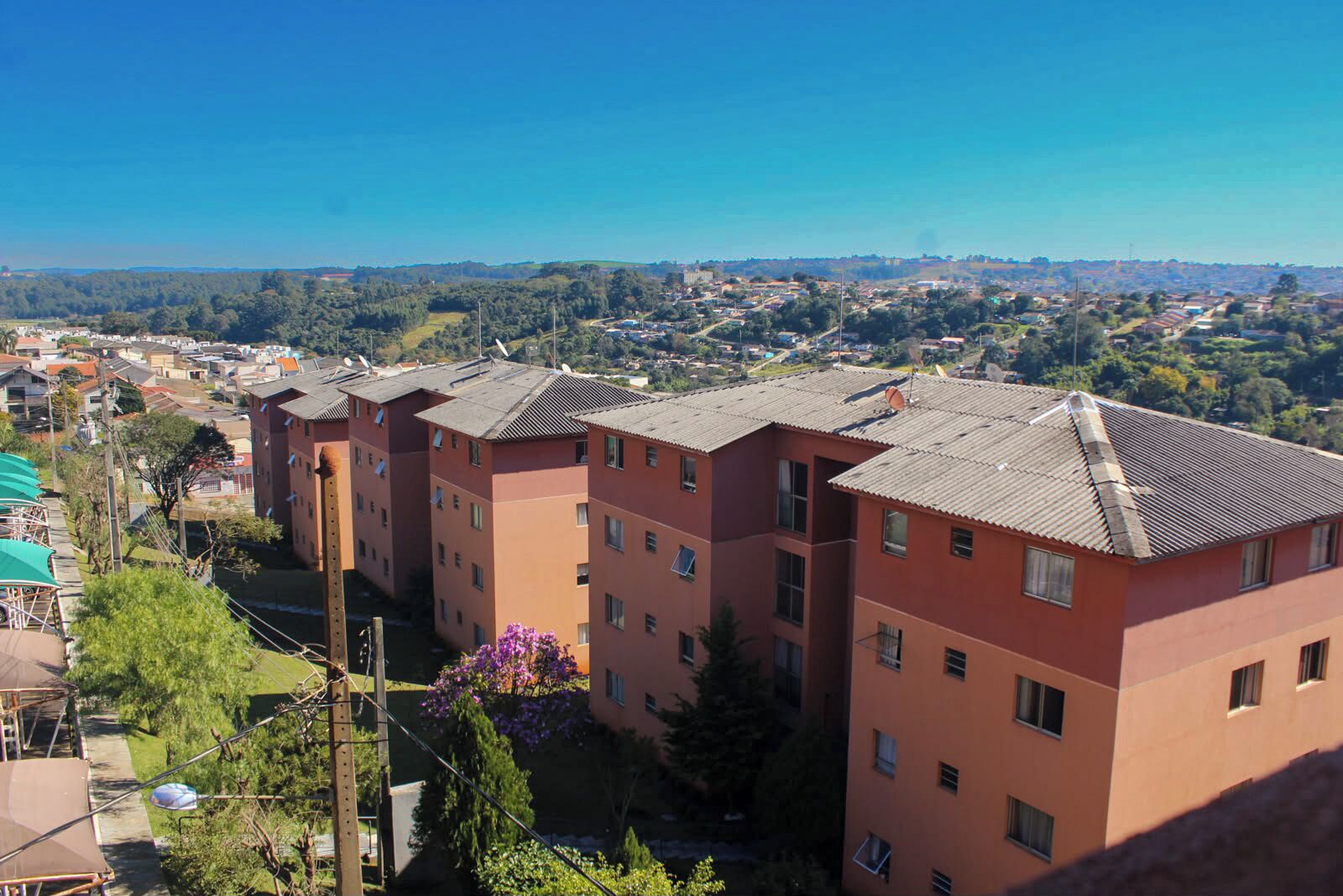A multi-story residential building with a flat roof, surrounded by greenery and a clear blue sky.