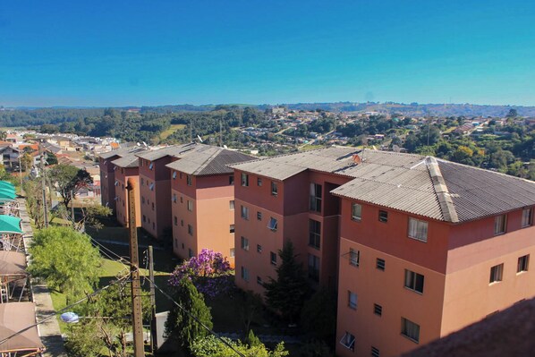 Un edificio residencial de varios pisos con techo plano, rodeado de vegetación y un cielo azul despejado.