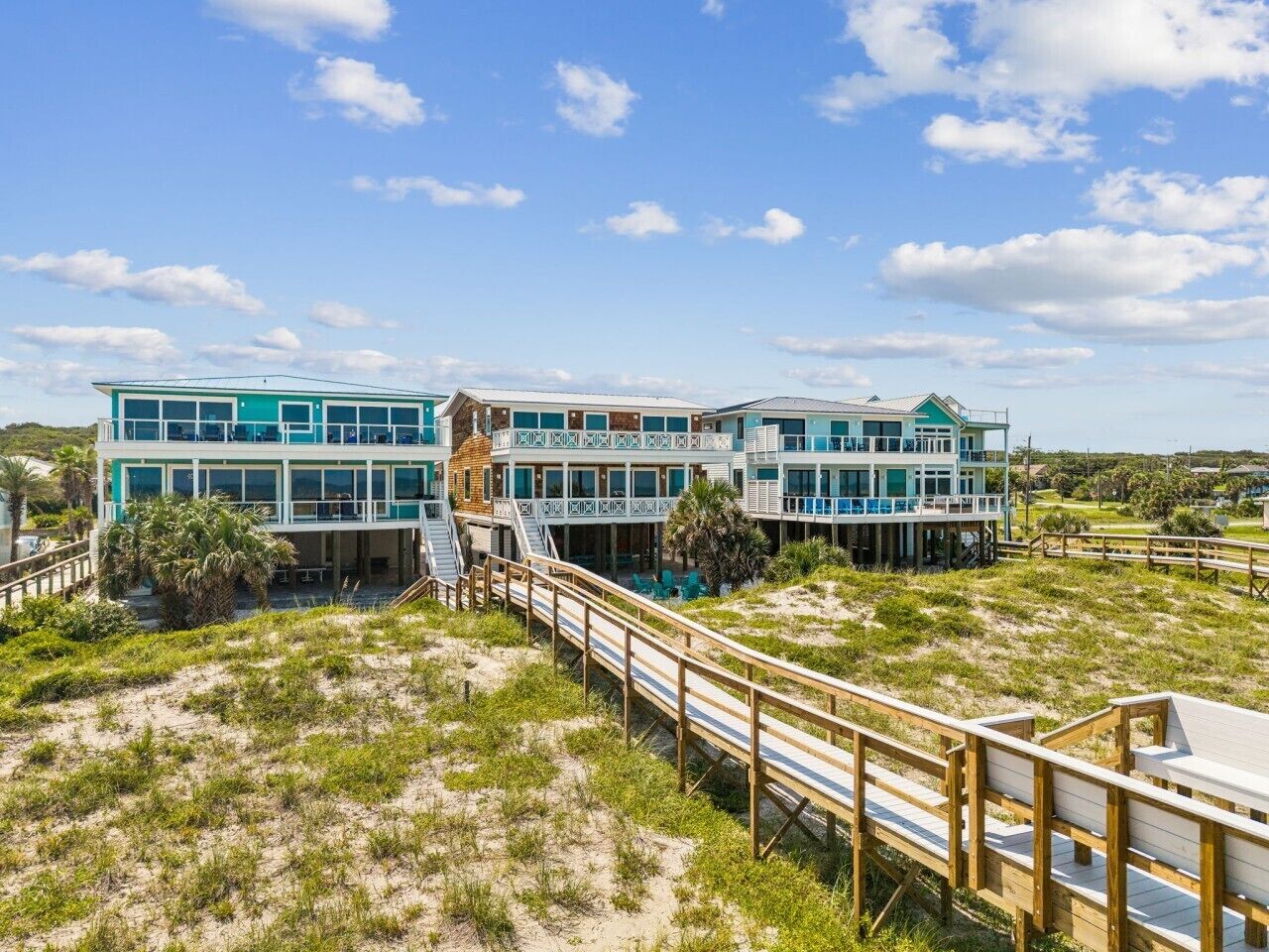 Une propriété située en bord de mer, avec une promenade en bois menant à un immeuble à plusieurs étages doté de grandes fenêtres.
