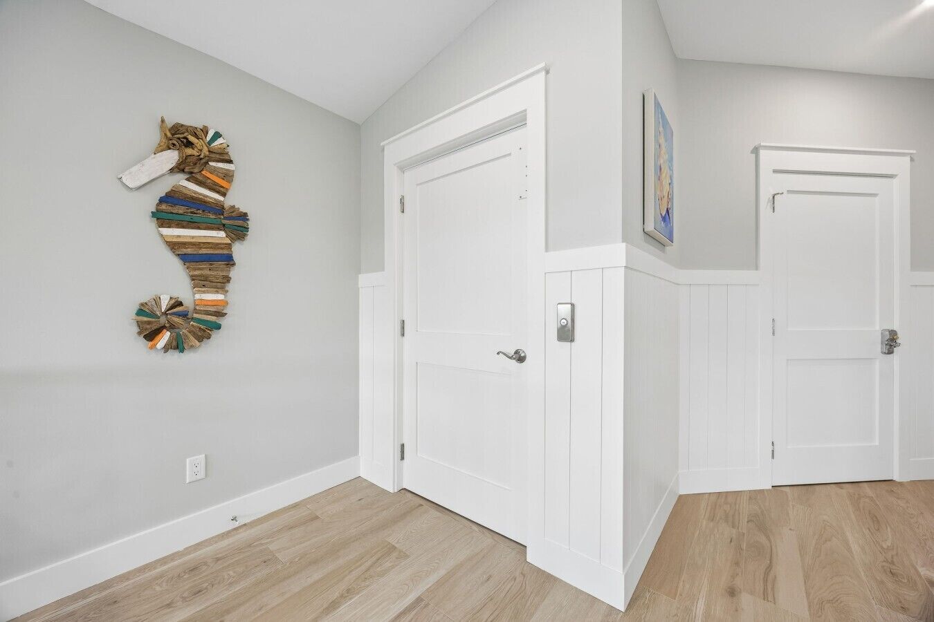 A hallway with white doors, a wooden floor, and a wall-mounted artwork.