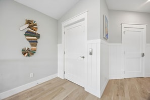 A hallway with white doors, a wooden floor, and a wall-mounted artwork.