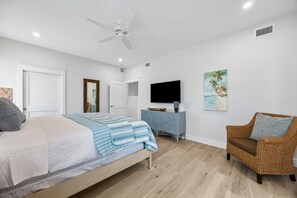 Un dormitorio con cama, una silla, televisión y obras de arte en la pared.