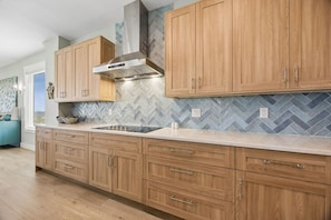 A kitchen with wooden cabinets, a stainless steel range hood, and a herringbone tile backsplash.
