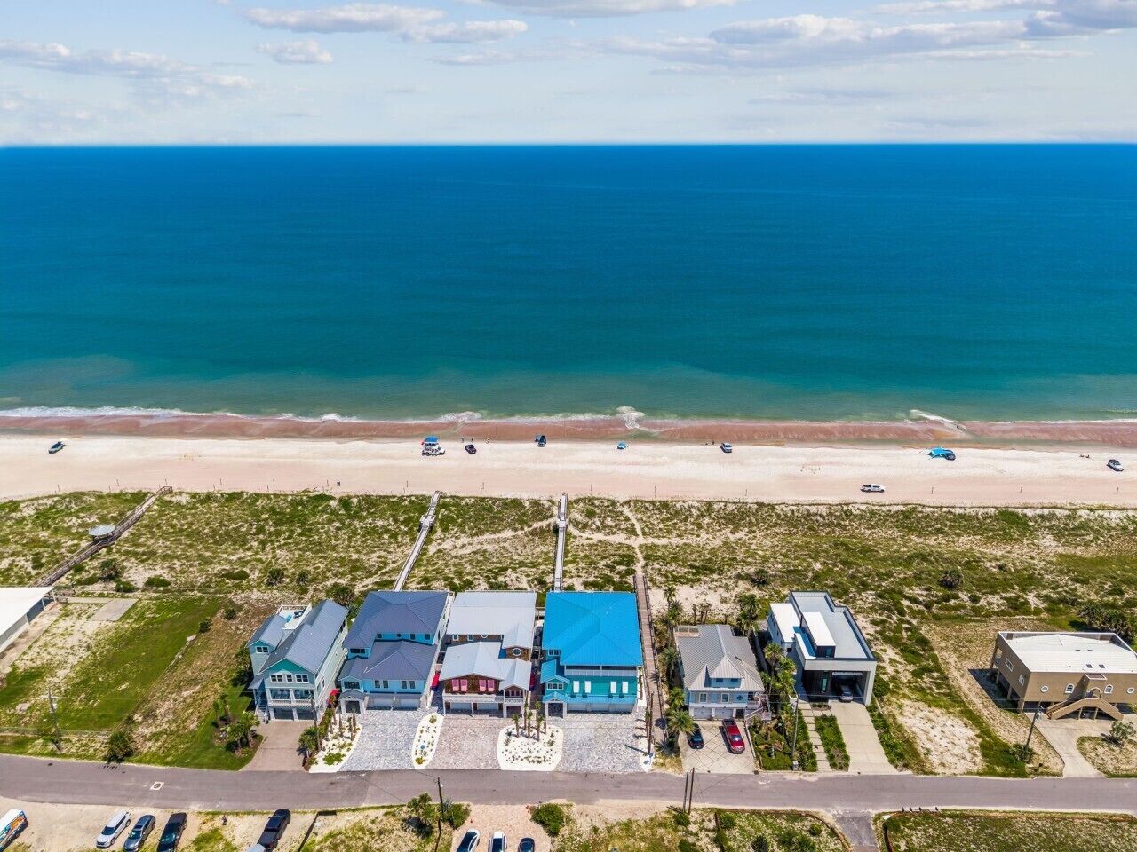 An aerial view of a coastal property with multiple buildings, a beach, and a road.