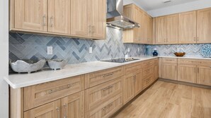A modern kitchen with wooden cabinets, a herringbone tile backsplash, and a stainless steel range hood. - Fin & Tonic | Brand New Oceanfront Beach House | Hot Tub | Elevator | EV Charger | Sleeps 18 (Fernandina Beach)