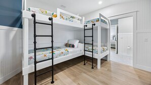 A bunk bed room with white walls, a wooden floor, and a door leading to another room. - Fin & Tonic | Brand New Oceanfront Beach House | Hot Tub | Elevator | EV Charger | Sleeps 18 (Fernandina Beach)