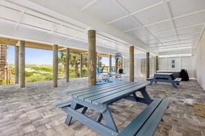 Un patio techado al aire libre con mesas de picnic, un ventilador y una hamaca.