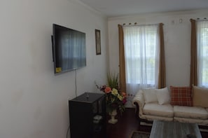 Ein Wohnzimmer mit Sofa, Couchtisch, Wandfernseher und einem Fenster mit Vorhängen.