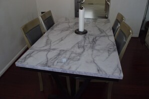 Uma mesa de jantar com tampo de mármore, quatro cadeiras e um pilar central.