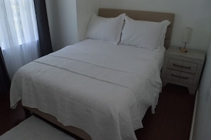 Ein ordentlich bezogenes Bett mit Kopfteil, ein Nachttisch mit Lampe und ein Holzboden.
