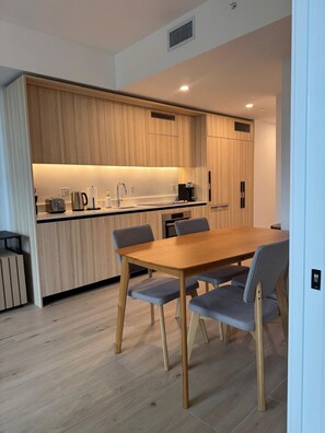 A modern kitchen with wooden cabinets, a built-in oven, and a dining area with a wooden table and chairs. - Spacious 1BR Condo in Downtown Miami | Sleep 4 (Miami)