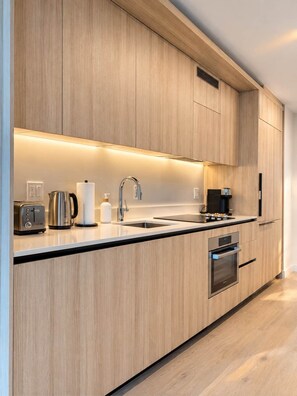 A modern kitchen with wooden cabinets, a stainless steel sink, a coffee machine, and a built-in oven. - Spacious 1BR Condo in Downtown Miami | Sleep 4  | Free Parking (Miami)