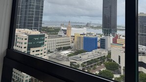 A view from a window overlooking a cityscape with various buildings, including high-rise structures and a construction crane. - Spacious 1BR Condo in Downtown Miami | Sleep 4 (Miami)