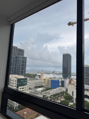 A view from a window overlooking a cityscape with various buildings, including high-rise structures and a construction crane. - Spacious 1BR Condo in Downtown Miami | Sleep 4 (Miami)
