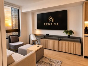 A modern living room with a sofa, a chair, a desk, and a television mounted on the wall displaying 'RENTIVA'. - Spacious 1BR Condo in Downtown Miami | Sleep 4  | Free Parking (Miami)