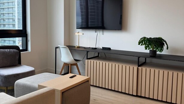 A modern living room with a flat-screen TV mounted on the wall, a sofa, a coffee table, and a potted plant. - Spacious 1BR Condo in Downtown Miami | Sleep 4 (Miami)