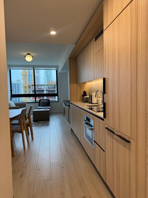 A modern kitchen with wooden cabinets, a built-in oven, and a window overlooking a construction site. - Spacious 1BR Condo in Downtown Miami | Sleep 4 (Miami)