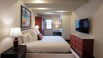 Quarto de hotel com cama, mesas de cabeceira, televisão, quadro e vista para o corredor.