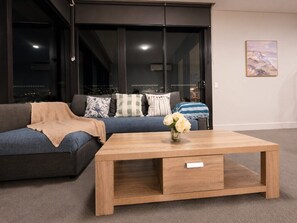A modern living room with a sofa, a coffee table, and a city view through large windows. - Sydney Olympic Park Panorama 3B2B by WinsonHome (Sydney Olympic Park)