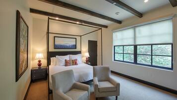 Quarto de hotel com cama de dossel, duas poltronas, uma janela ampla com vista e um quadro na parede.
