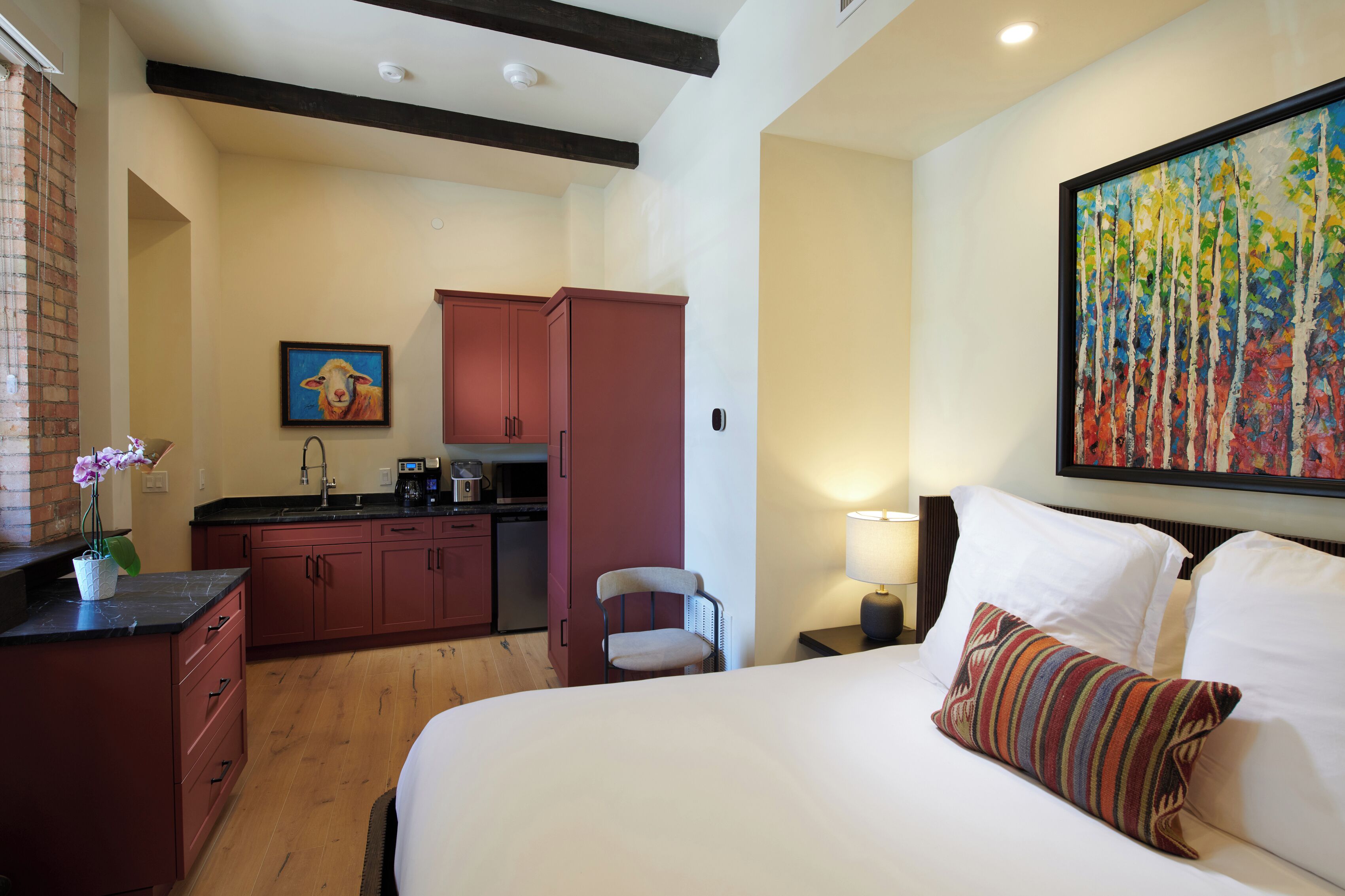 Une chambre d’hôtel avec un lit, un bureau, une chaise, une petite kitchenette et un tableau au mur.