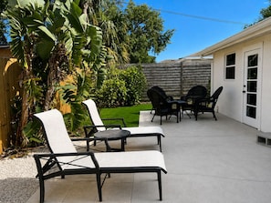 An outdoor patio area with a table and chairs, surrounded by a wooden fence and lush greenery. - Newly refurbished, private home with open layout and backyard (Sarasota)