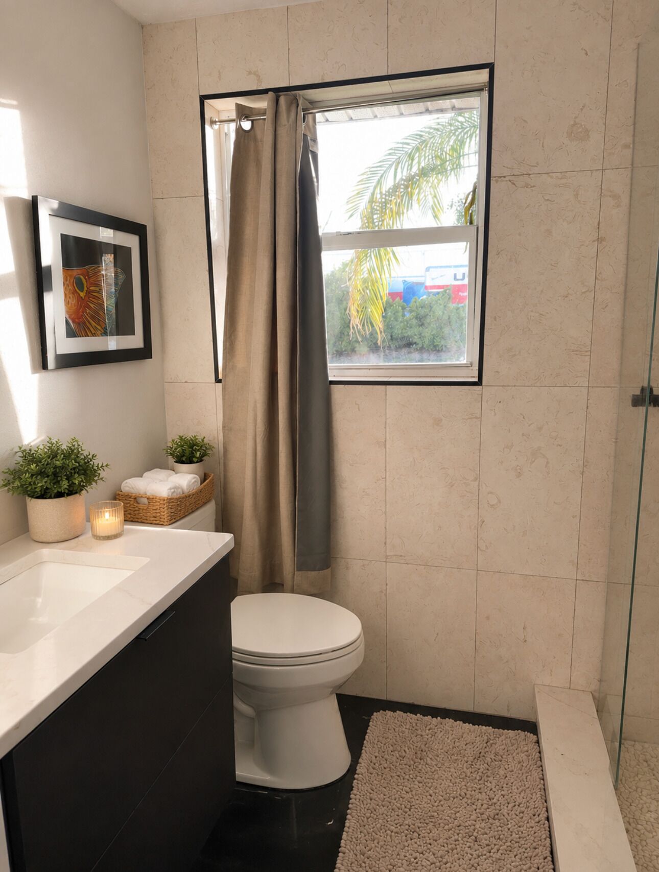 Ein modernes Badezimmer mit Toilette, Waschbecken, Dusche, einem Fenster mit Blick und einem gerahmten Bild an der Wand.