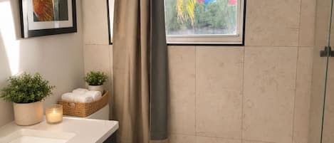 Un baño moderno con inodoro, lavamanos, ducha, ventana con vistas y un cuadro en la pared.