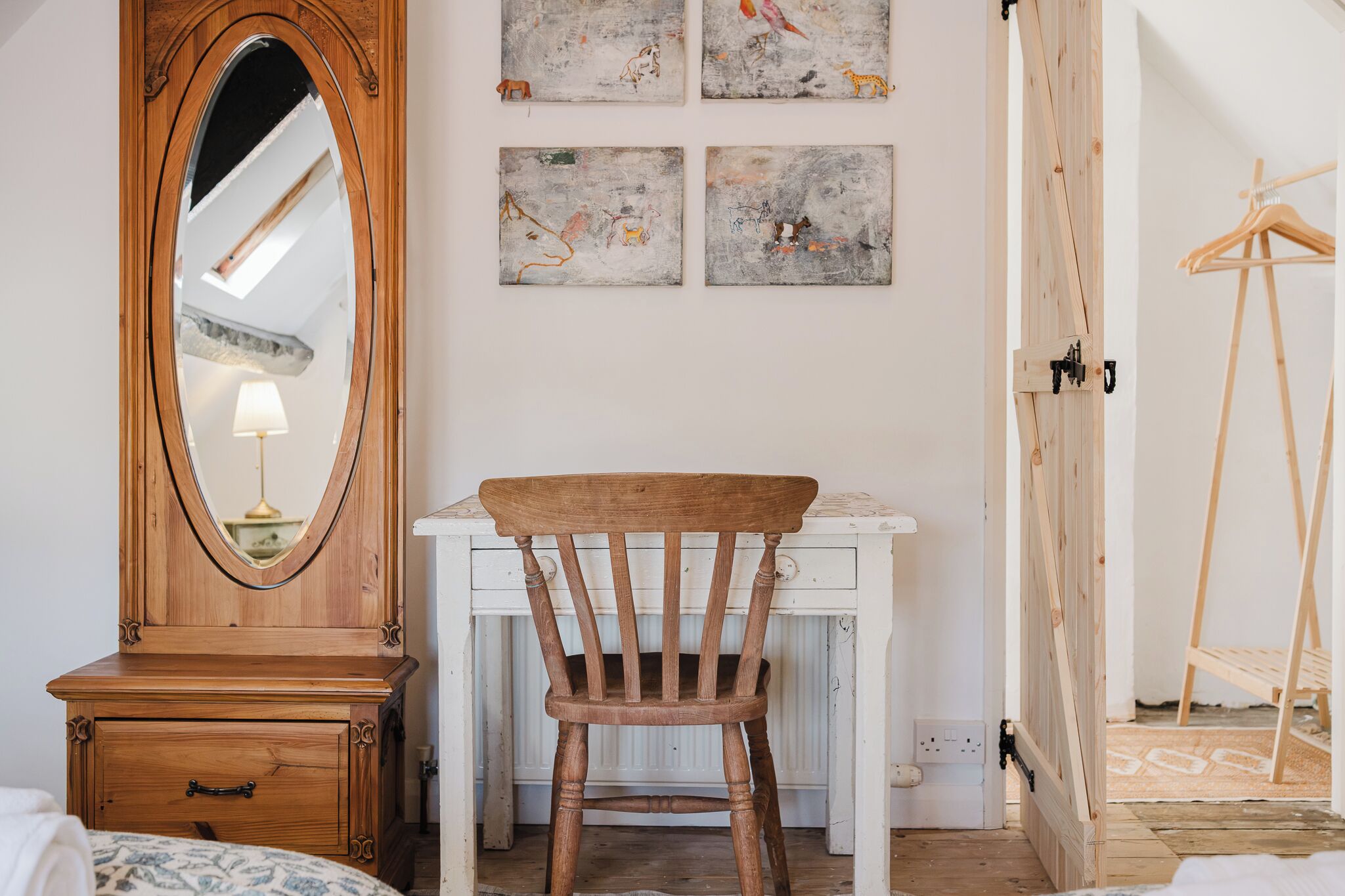 Un dormitorio con un aparador de madera, un escritorio, una silla y una cama. Se observan obras de arte en la pared y un armario de madera.