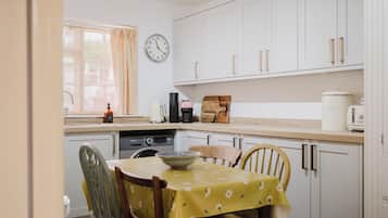 A kitchen with white cabinets, a clock, a toaster, a kettle, and a table with chairs.