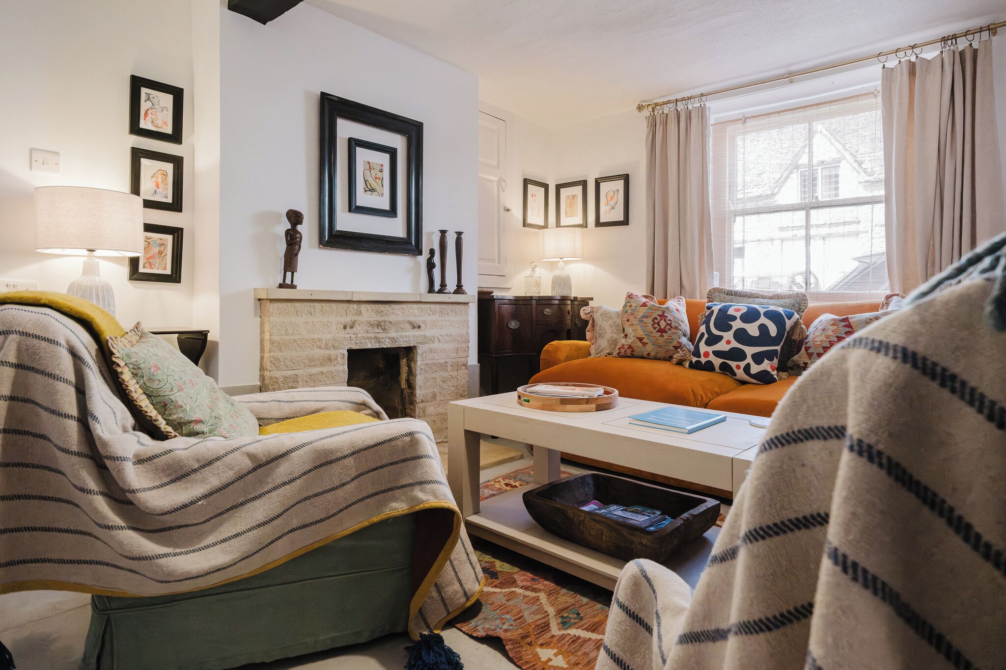A cozy living room with a fireplace, a sofa, a coffee table, and a window with curtains.